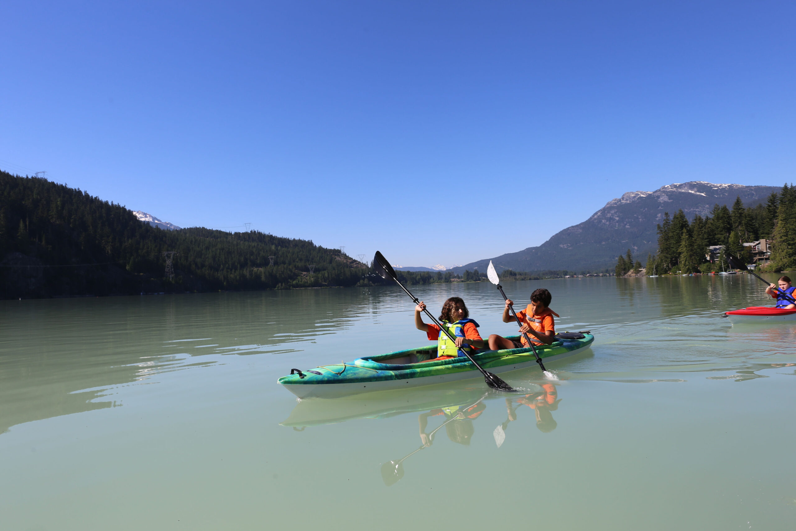 Adventure camp in Whistler during a summer camp in Canada. We see two campers on a kayak on a pristine lake